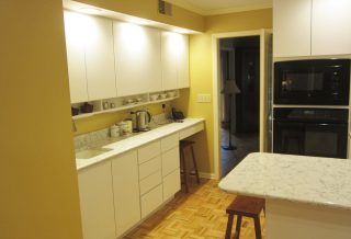 Kitchen remodel in Champaign IL includes a tea and coffee nook, contemporary cabinets, quartz countertops, new range hood, and decorative glass tile.