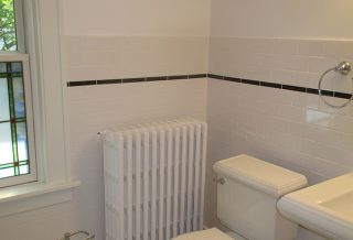 1920s bathroom remodel includes the original hex tile flooring, stained glass window, and radiator.